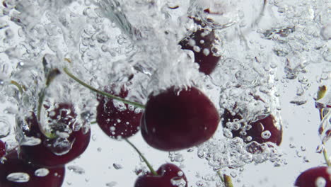 ripe cherries falling water making splashes bubbles at white background close up