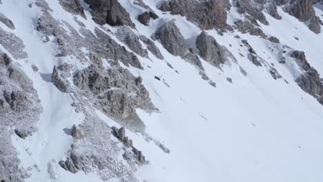 Drone-shot-panning-sideways-of-snowy-hillside-with-rocks-in-the-Italian-alps