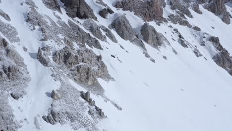 Disparo-De-Drones-Panoramización-Lateral-De-Ladera-Nevada-Con-Rocas-En-Los-Alpes-Italianos