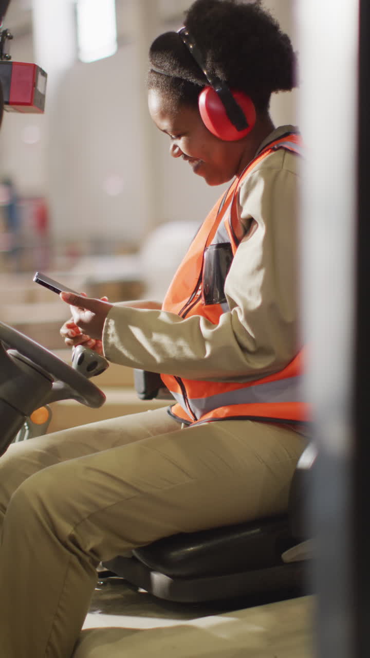 Vertical video of happy african american female worker using smartphone in warehouse