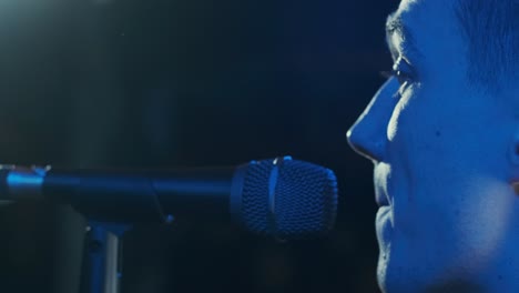 man singing song in microphone during performance on stage on rock concert. close up man rock star singer on music concert on colorful light background