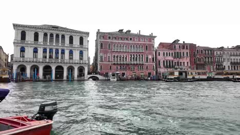 Static-view-of-gondolas-gliding-through-the-water-past-colorful-historic-buildings-in-Venice,-Italy