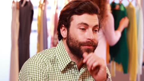 bored man sitting while woman selecting clothes from clothes rail