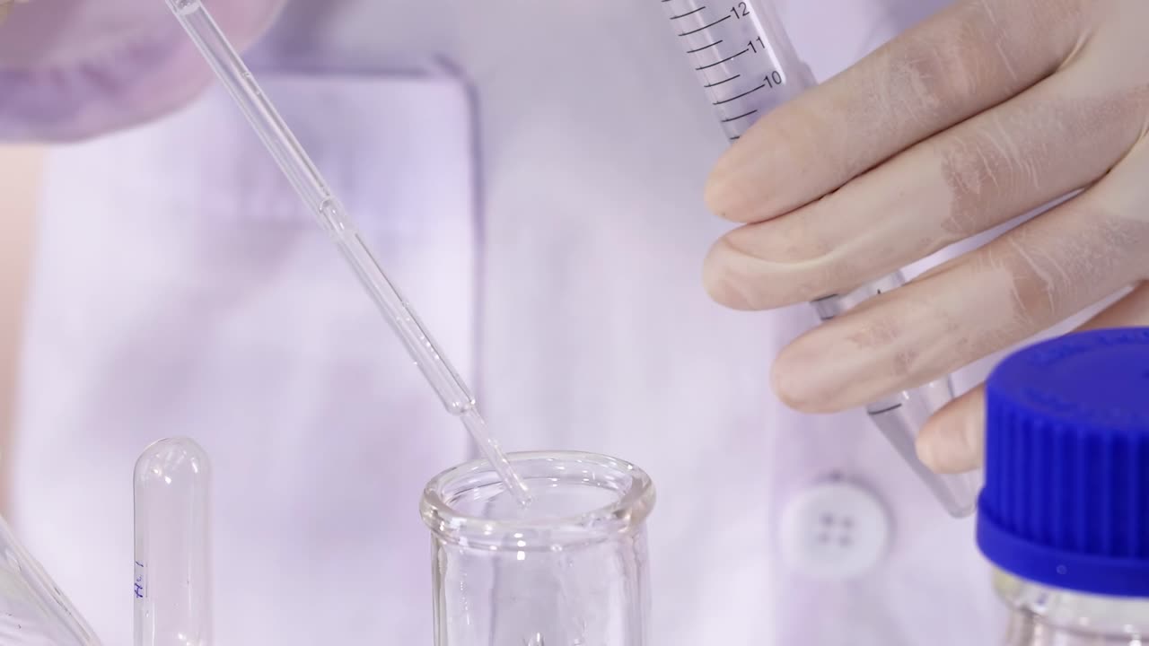 Close-up of hands using a pipette to mix pink solution in a lab setting.
