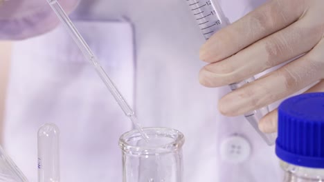 close-up of hands using a pipette to mix pink solution in a lab setting.