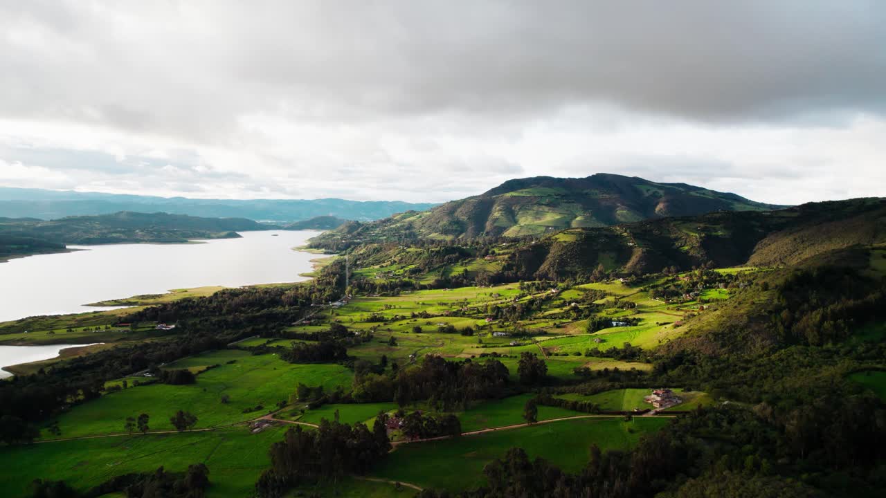 Aerial zoom in shot capturing Guatavita’s rich green valleys and sparkling lake under a dramatic sky