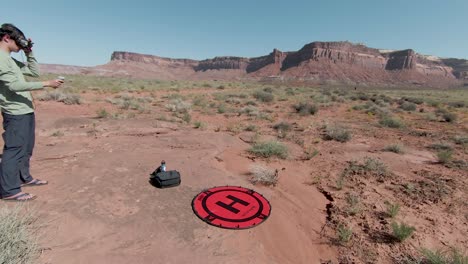 FPV-Flugzeugbetreiber-Landet-Die-Drohne-An-Einem-Sonnigen-Tag-Mitten-In-Der-Roten-Felsenwüste-Mit-Einigen-Klippen-Im-Hintergrund