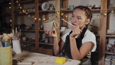 young woman potter smoothing out the clay cup using a wet brush