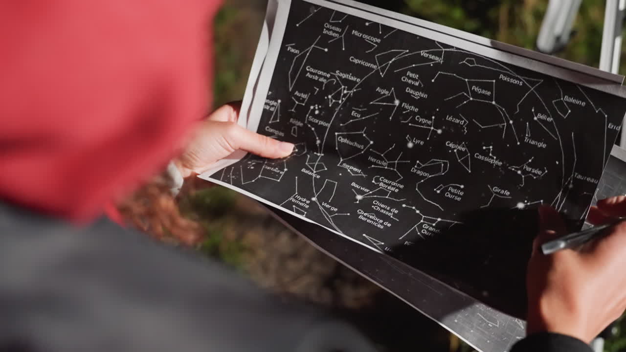 closeup star chart held outdoors by astronomer marking constellations with pen near telescope tripod, autumn grass background, hands tracing celestial patterns, tactile mapping, night preparation