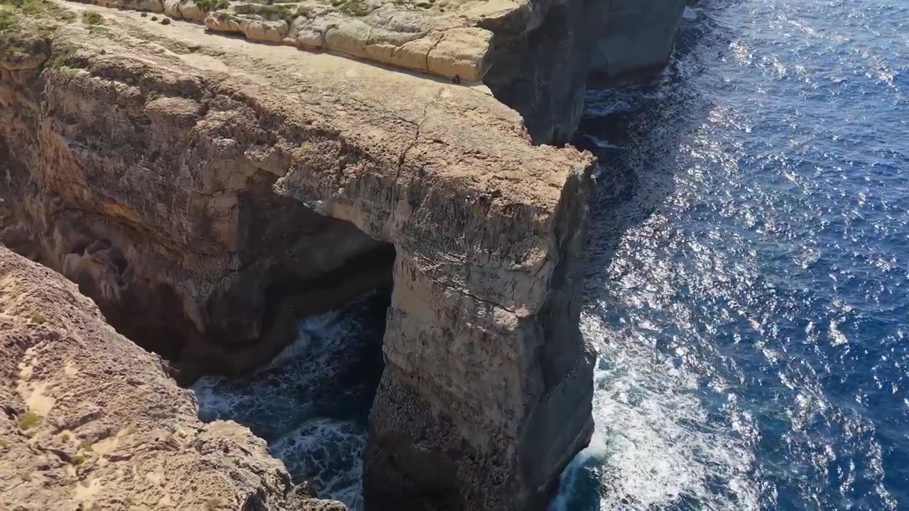 Wied il-Mielaħ natural arch in Gozo, Malta, above rugged sea cliffs and blue Mediterranean water along the rocky coastline, scenic island landscape in aerial view.