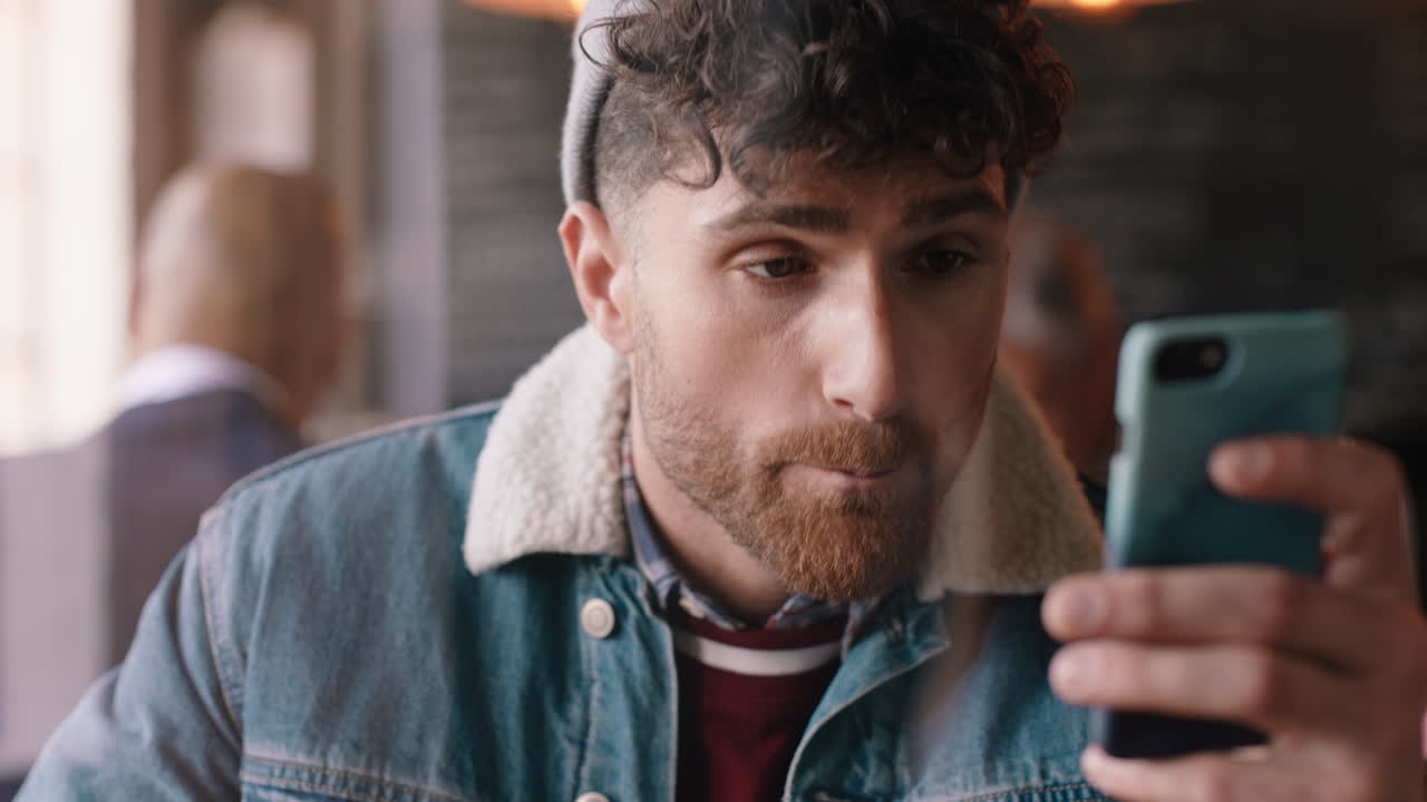 hombre hipster atractivo que usa un teléfono inteligente en un café bebiendo café enviando mensajes de texto compartiendo mensajes en las redes sociales disfrutando de la tecnología móvil