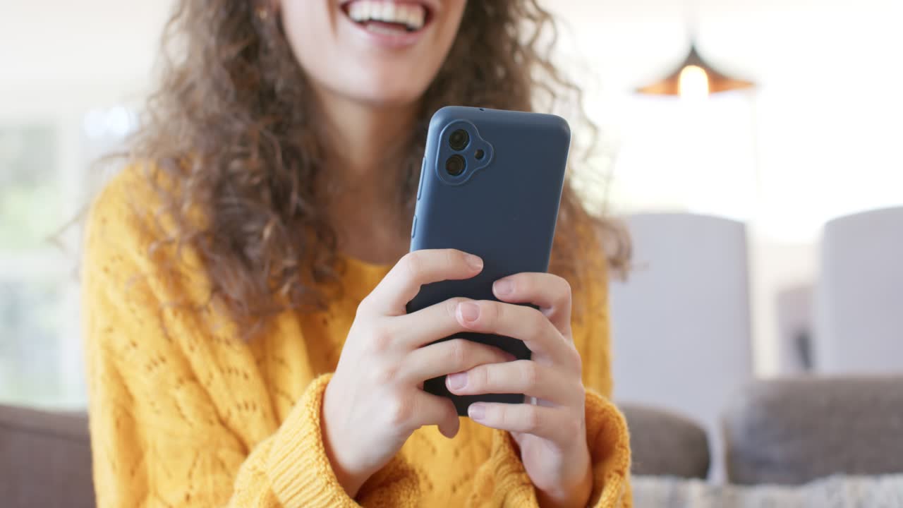 Depois que a tela do celular se ilumina, uma mulher sorri enquanto toca e rola a tela, olhando uma mensagem no sofá perto da janela