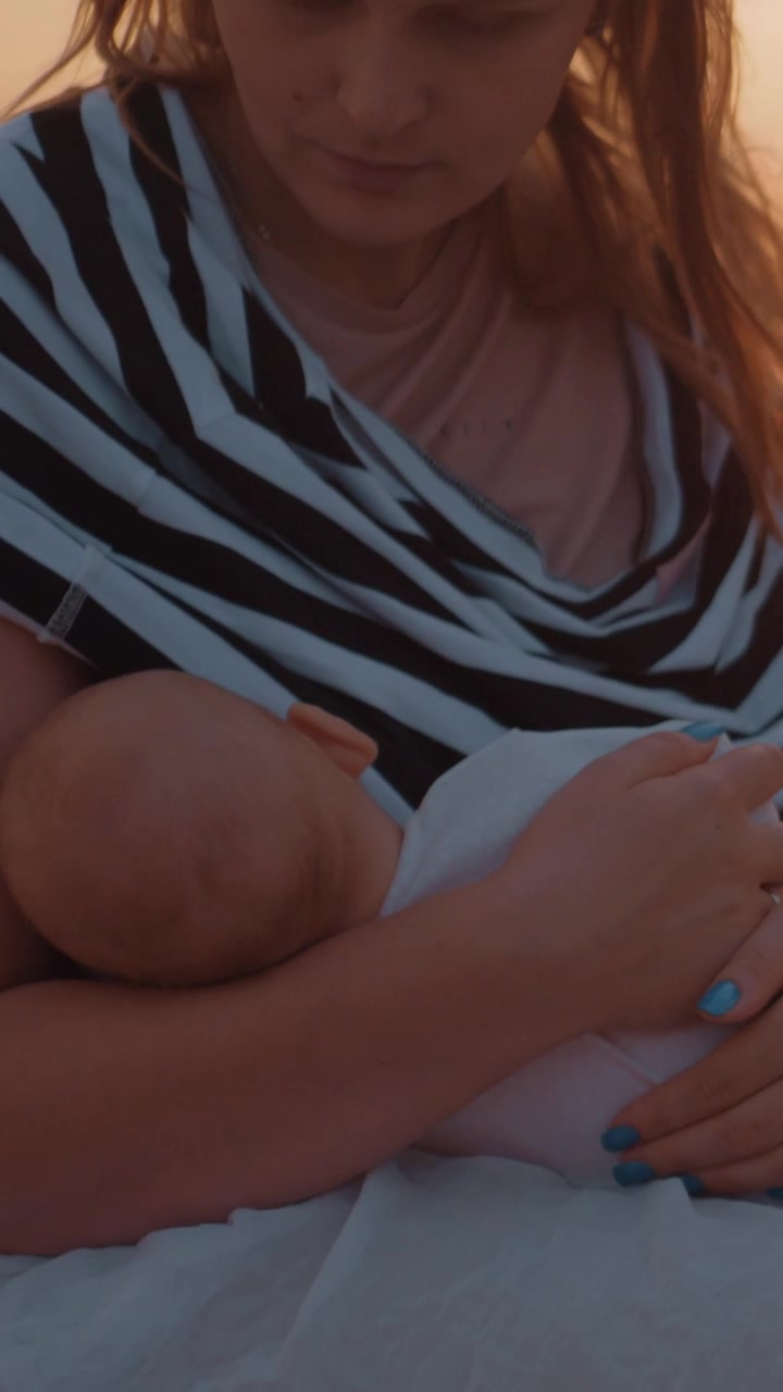 Mother nursing and caressing baby sitting on the pier at sunset