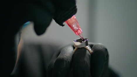 tattoo needle loading ink in salon closeup. hands holding permanent paint jar