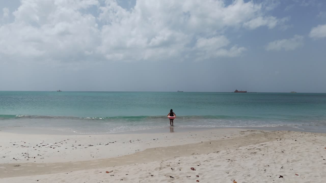 Woman in swimsuit running toward turquoise sea between two trees on Fort James Beach in daylight