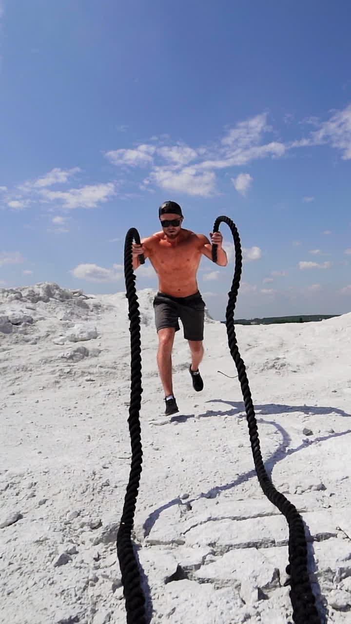 Athlete doing cross fitness workout outdoor. Battle rope training as functional fitness on nature Vertical video