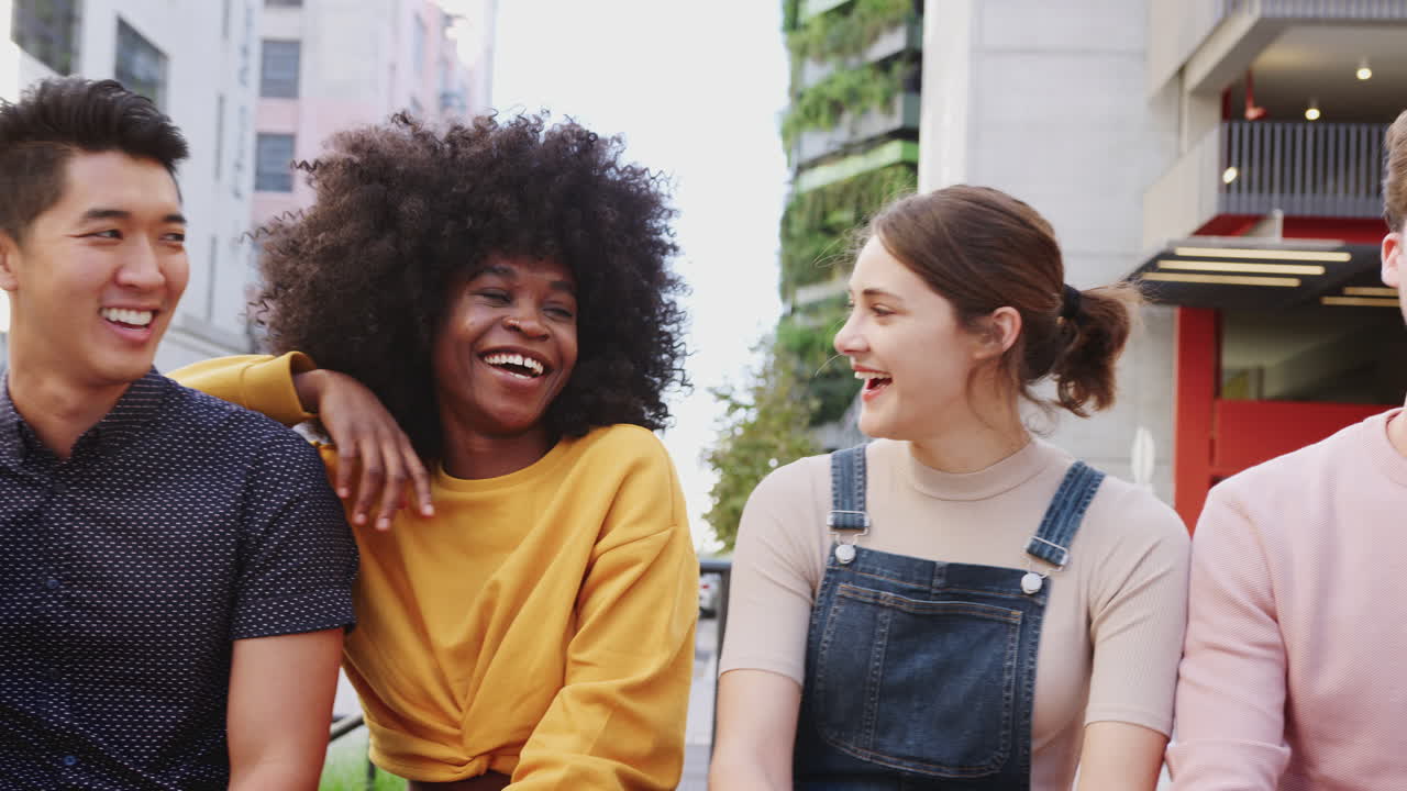 Six young adult multi-ethnic friends in a row on a city street laughing, waist up, panning shot