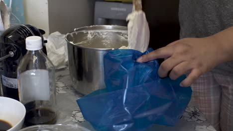 Baker-Carefully-Filling-Blue-Piping-Bag-With-Fresh-Cream-In-Kitchen