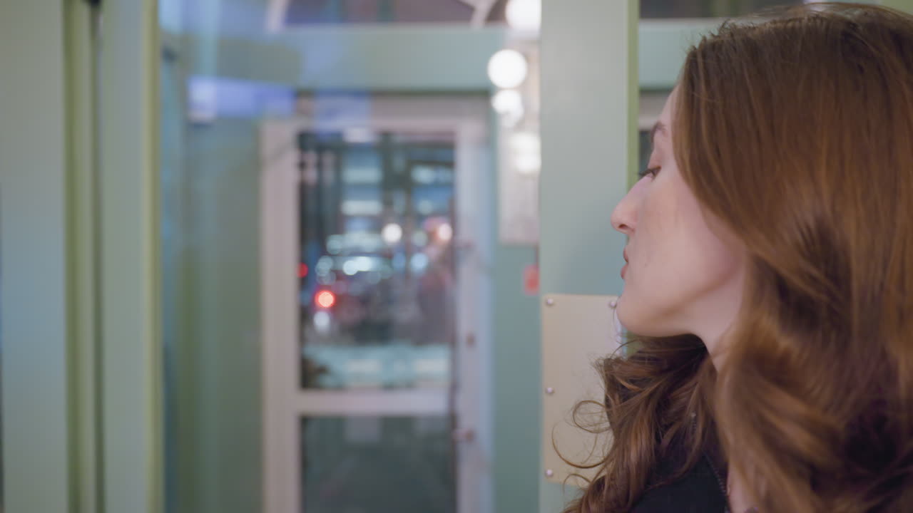 Lady in black outfit confidently walking forward while opening glass door, framed by modern interior with lights and reflections visible in background as door begins to close behind her
