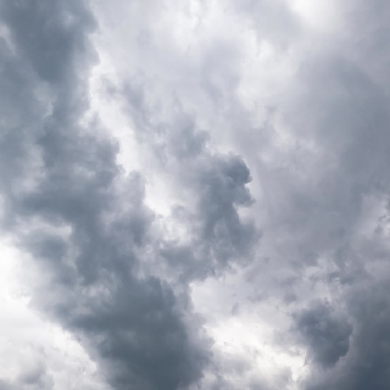 White fluffy cumulus clouds quickly changing shape in the blue skies. Grey cloudscape appearing and covering the sky. View from below timelapse