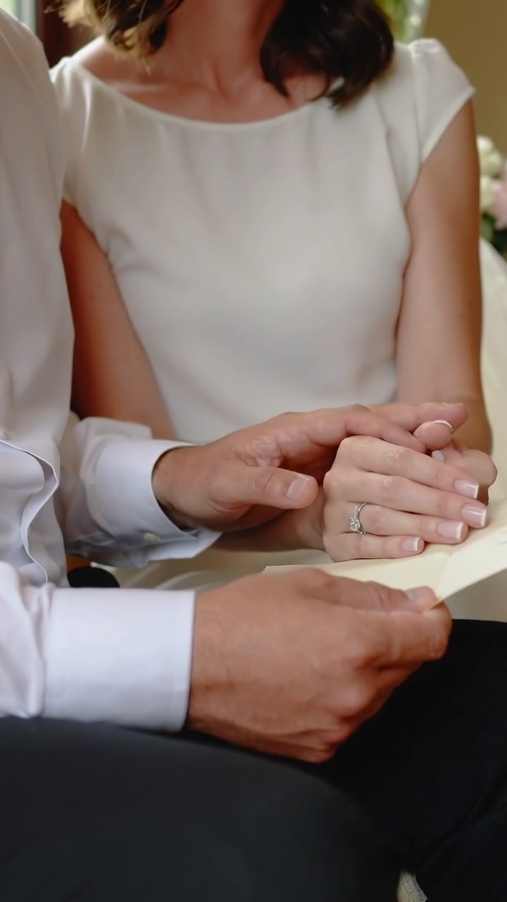 Vertical video: Opening man in bowtie reading cream card at ceremony, touching her ringed hand