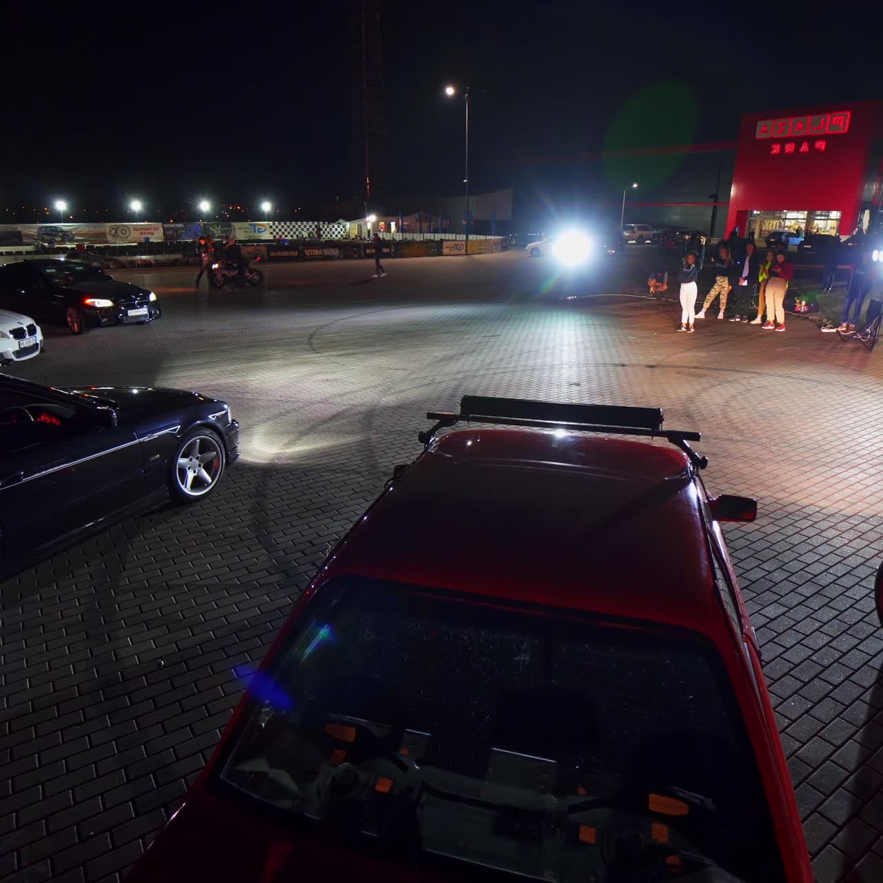 Youngsters leave their cars driving seat and walking forward. Group of standing at backdrop. Square at night as backdrop