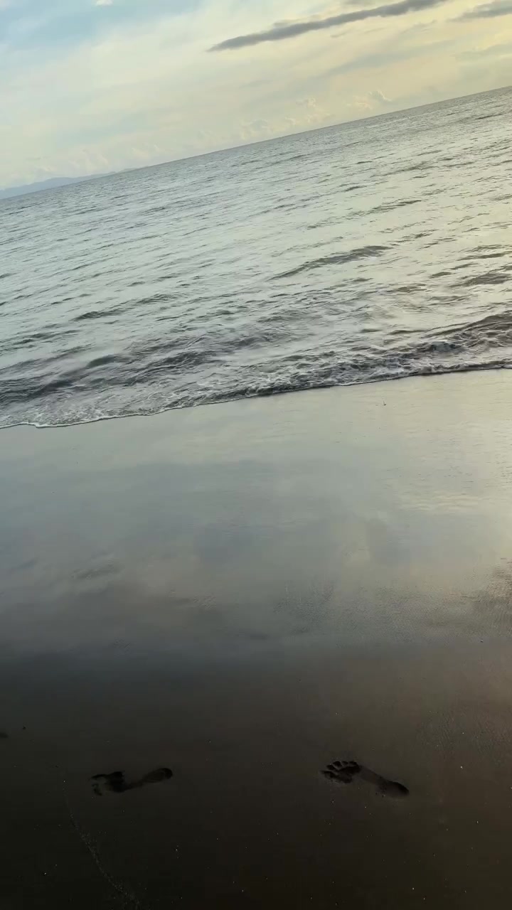 Peaceful Ocean Waves Washing Over Footprints on a Sandy Beach