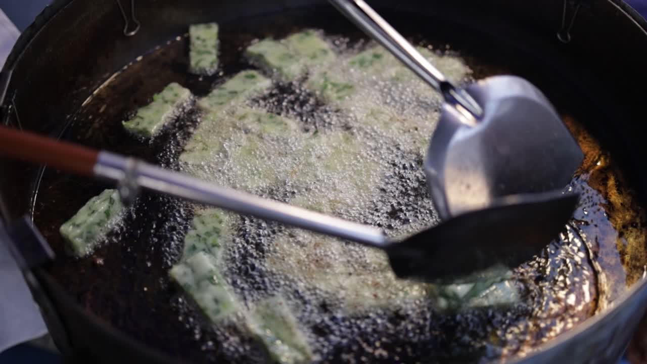Food vendor at a food center cooking Fried Chinese chive dumplings in hot boiling oil in a frying pan