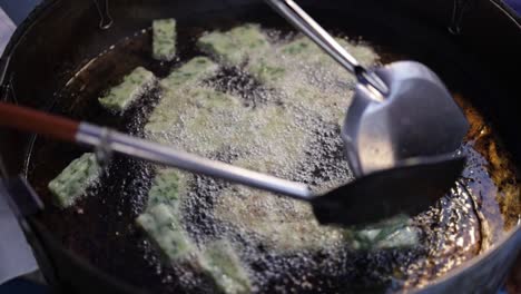 food vendor at a food center cooking fried chinese chive dumplings in hot boiling oil in a frying pan