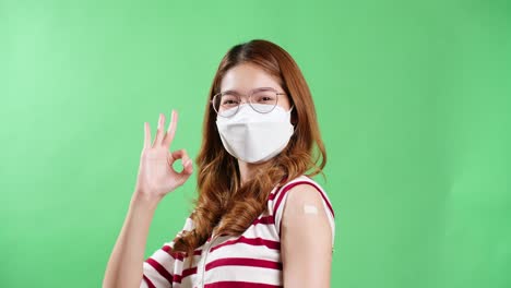 Young-Asian-woman-pointing-to-her-arm-after-being-vaccinated-against-covid-19-in-studio-with-chroma-key-background