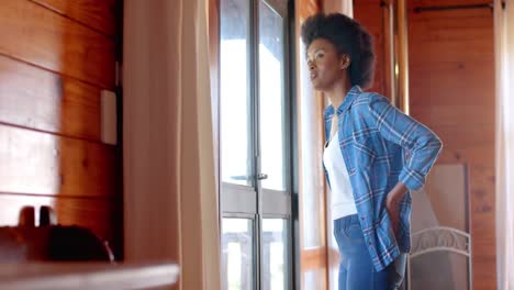 happy african american woman looking out window in living room, in slow motion
