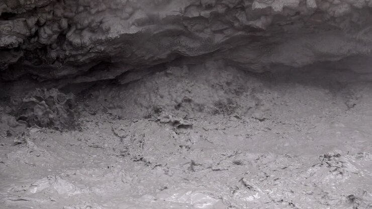 Nærbillede af vand fra geotermisk mudderpøl, der eksploderer i slow motion under udhæng fra en muddervulkan