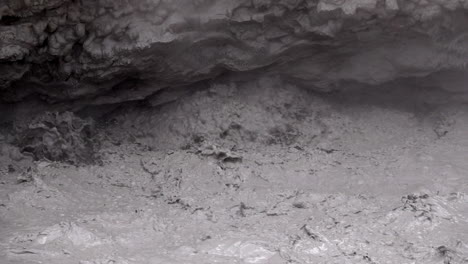 close-up of geothermal mud pot water exploding in slow motion under mud volcano overhang