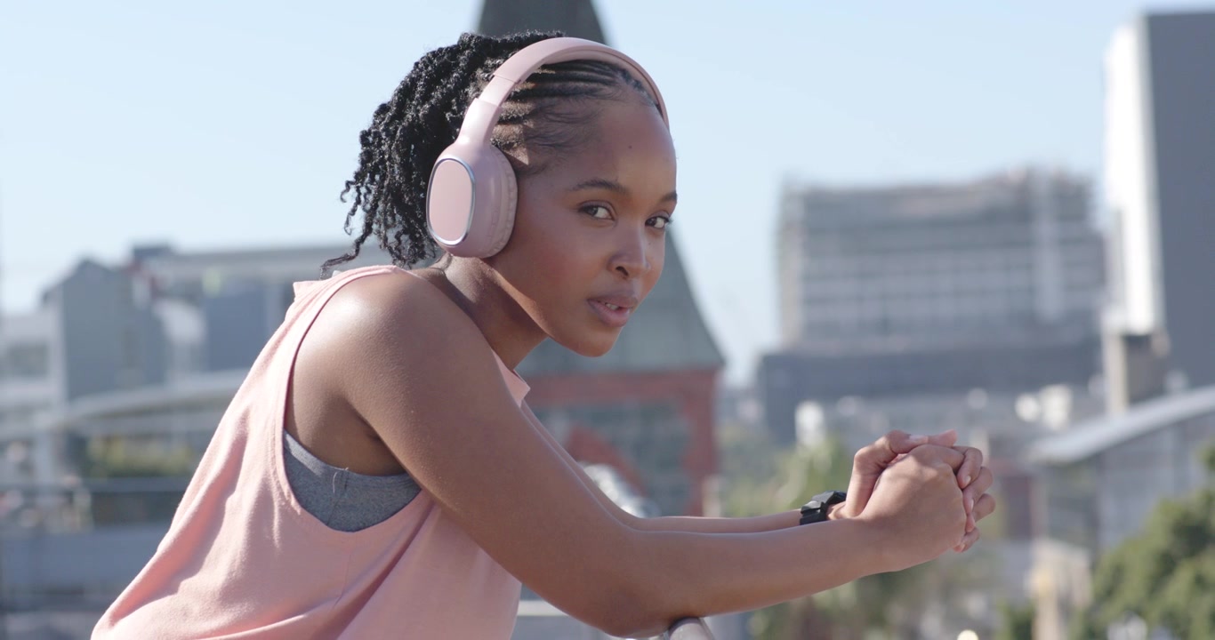 African woman entering checking watch leaning on roof rail in pink headphones listening to skyline