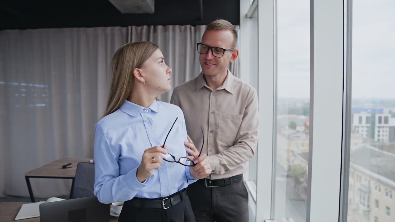 Colleagues at work communicate comforting and supporting each other. Male employee proposing help to a lady feeling bad. Office indoors backdrop.