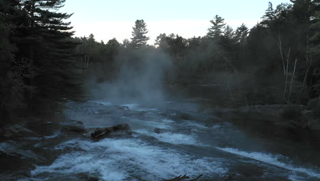 un dron aéreo disparó río arriba sobre una cascada de un bosque oscuro y brumoso al atardecer con árboles en silueta