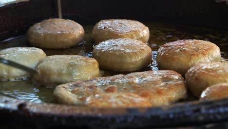 Xian-Bing-Recién-Hecho-Cocinando-En-Una-Sartén-De-Aceite-Caliente,-Un-Vendedor-Volteando-Una-Sabrosa-Masa-De-Pastel-De-Carne-De-Cerdo-Picada-Usando-Pinzas-De-Cocina,-Friendo-Hasta-Que-Se-Dore,-Primer-Plano-De-Comida-Asiática-Popular