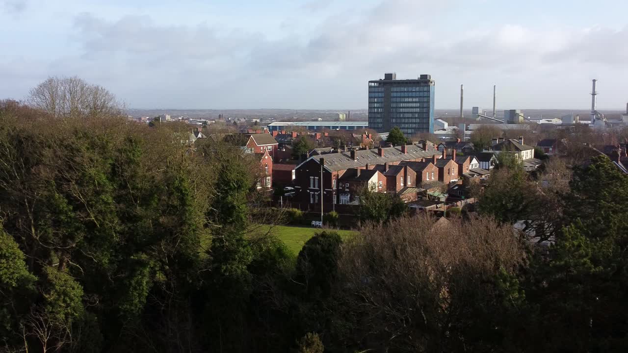 vista aérea que se eleva por encima de los árboles del parque hasta el paisaje urbano industrial con rascacielos azules, merseyside, inglaterra