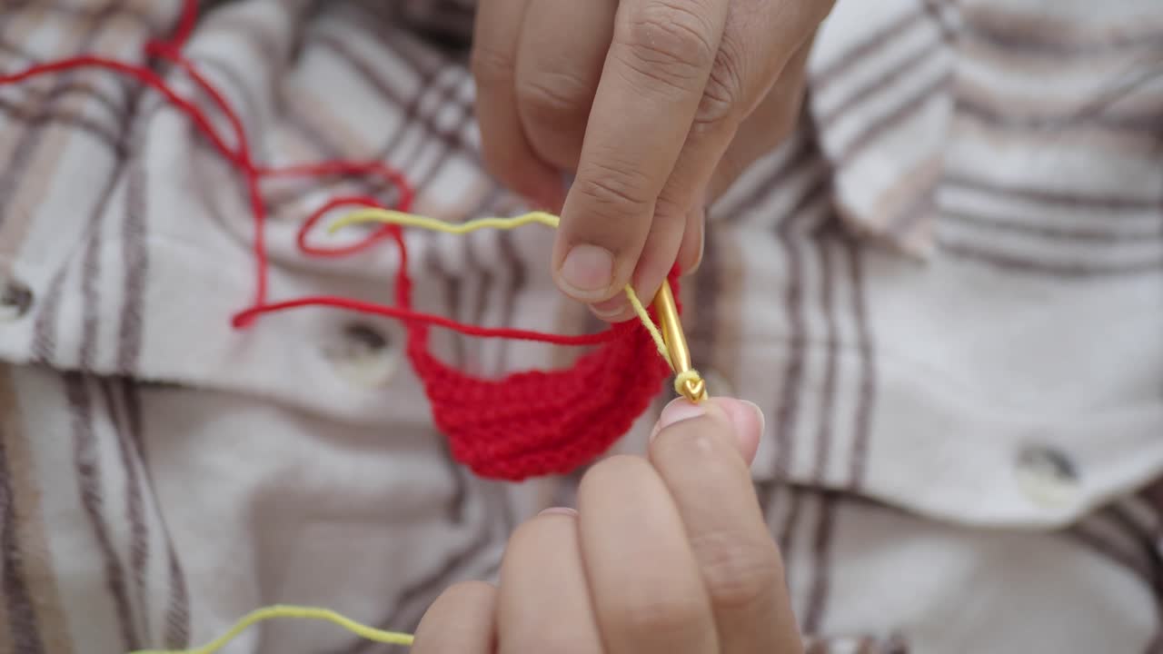 Close-up of hands crocheting with red and yellow yarn