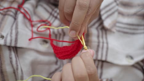 close-up of hands crocheting with red and yellow yarn