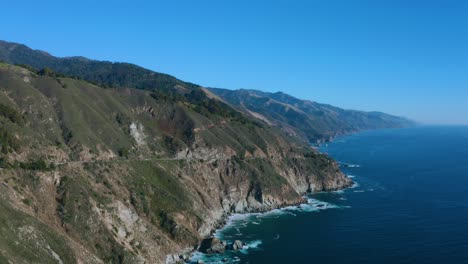 aerial over the pacific ocean with a small highway cutting through the mountainside.