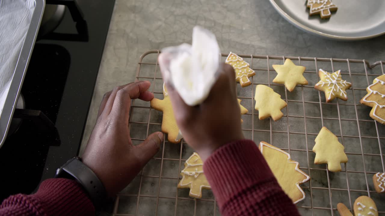 African American man placing gingerbread cookie piping icing with bag decorating shapes in kitchen