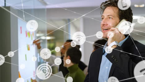 animación de una red de iconos digitales sobre un hombre de negocios caucásico hablando en su teléfono inteligente en la oficina.
