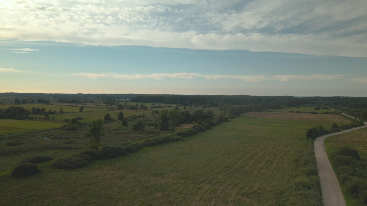 Flyver over grønne enge og landbrugsarealer med skov i baggrunden