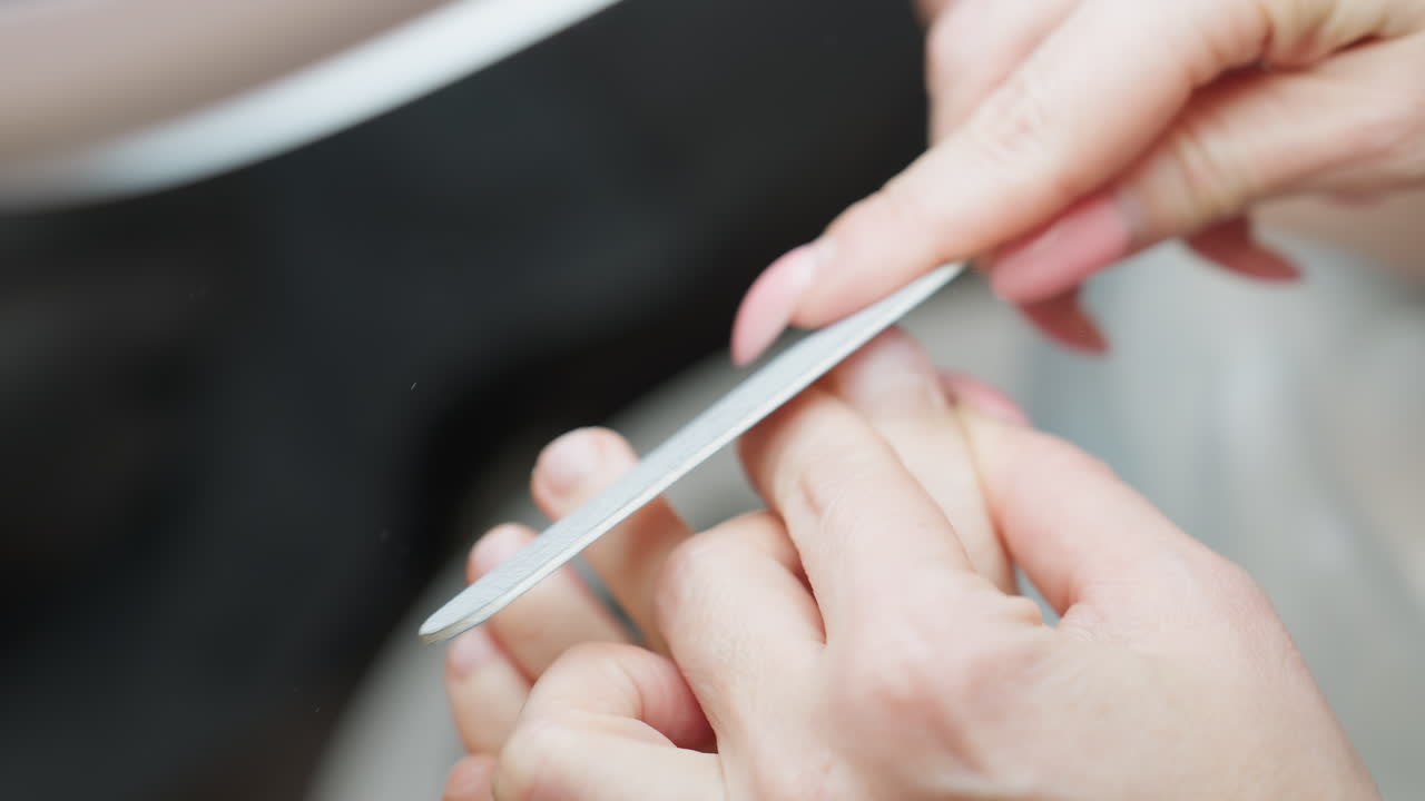 Closeup view of client carefully filing big toenail with nail file during pedicure session, showing focus on self-care and grooming, with hands in clear focus and blurred background for depth