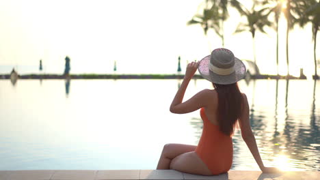 De-Vuelta-A-La-Cámara,-Una-Mujer-Sentada-Al-Borde-De-Una-Piscina-Se-Acerca-Para-Ajustarse-El-Sombrero-Para-El-Sol