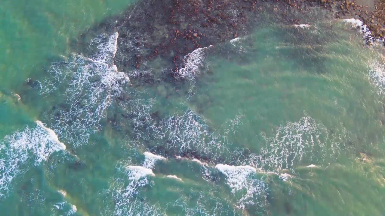 Calm waves from turquoise ocean hits rocky surface