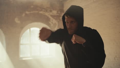 a man with curly hair in a black sports uniform from practicing air strikes in a sunny gym. boxing training