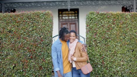 portrait of happy african american couple embracing and standing outside house, slow motion