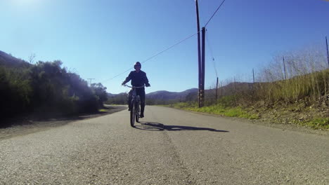 A-leather-clad-man-rides-a-motorized-bicycle-through-the-countryside-on-a-two-lane-road-2